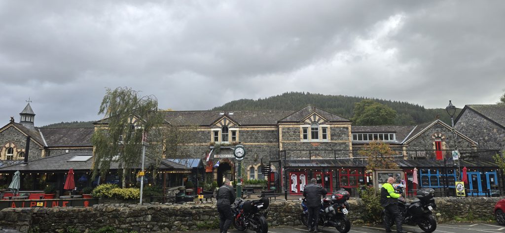 Betws-y-Coed village centre in Snowdonia North Wales with stone buildings, shops, and forested hills beneath dramatic clouds