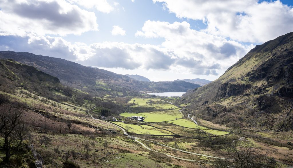 Mountain valley landscape in Snowdonia North Wales with winding road, green fields, lake, and dramatic clouds