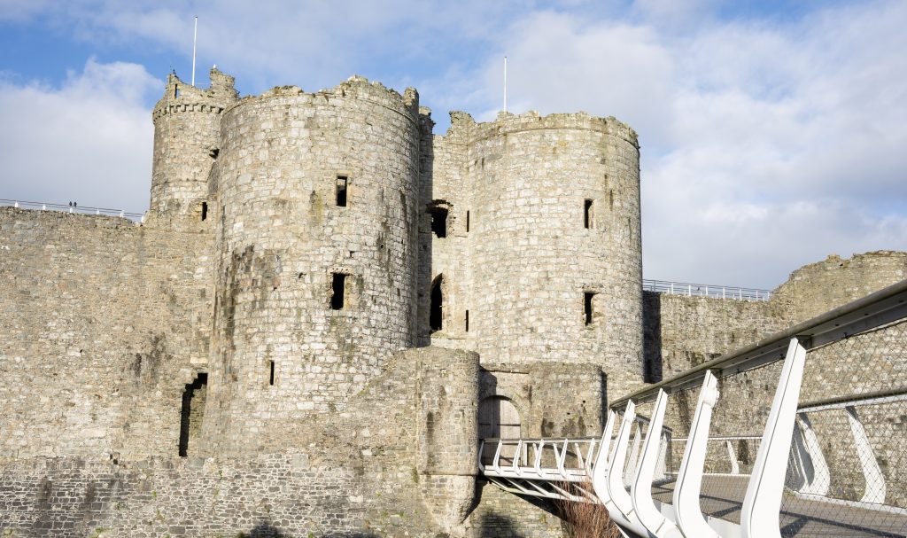 Harlech Castle in Snowdonia North Wales with ancient stone towers and modern footbridge under a blue sky