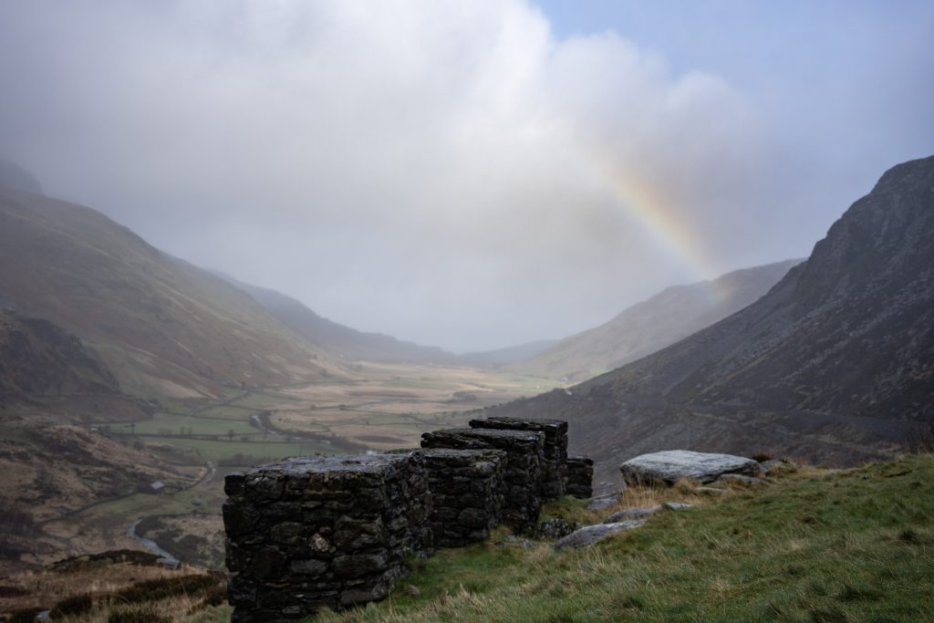 Rainbow over mountain valley near Llyn Ogwen in Snowdonia North Wales with stone ruins and dramatic misty landscape