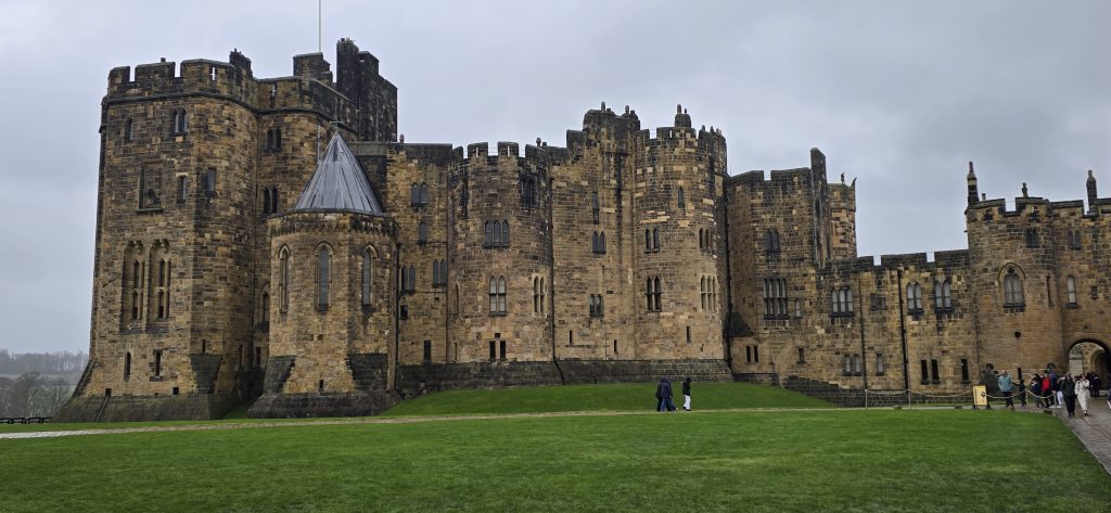 Alnwick Castle in Northumberland standing beneath grey skies, with medieval stone towers, historic architecture and green lawns surrounding one of England’s most iconic castle