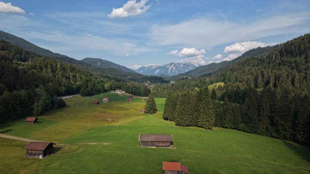 Aerial view of a green valley and scattered farm buildings beneath the Bavarian Alps